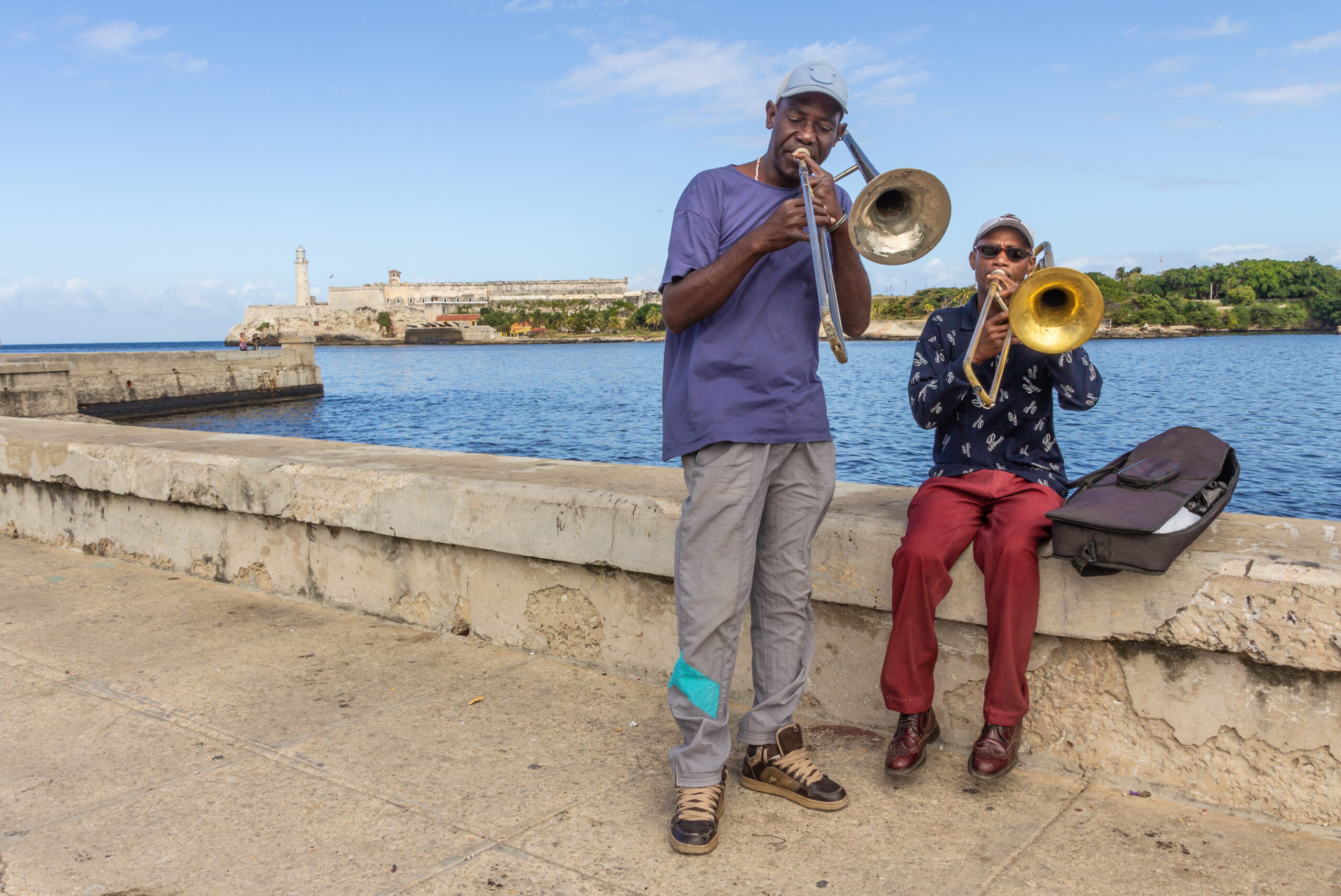 Havana, Cuba - November, 22 2012: Two ethnic street musicians playing trombones on shabby city embankment near beautiful river on sunny day