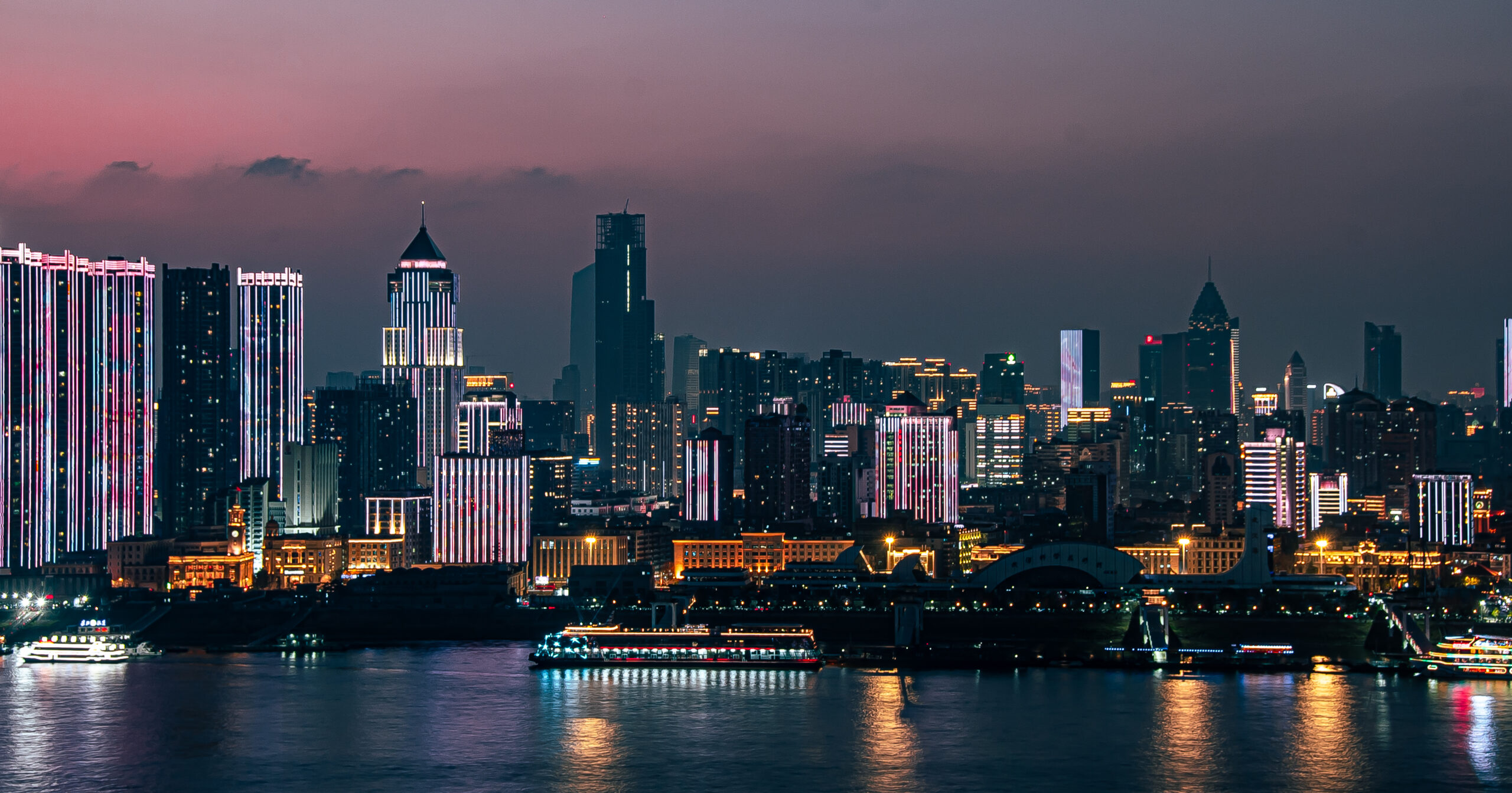 At night, by the Yangtze River, under the sunset, skyscrapers in Wuhan are illuminated, and ships are parked on the river surface