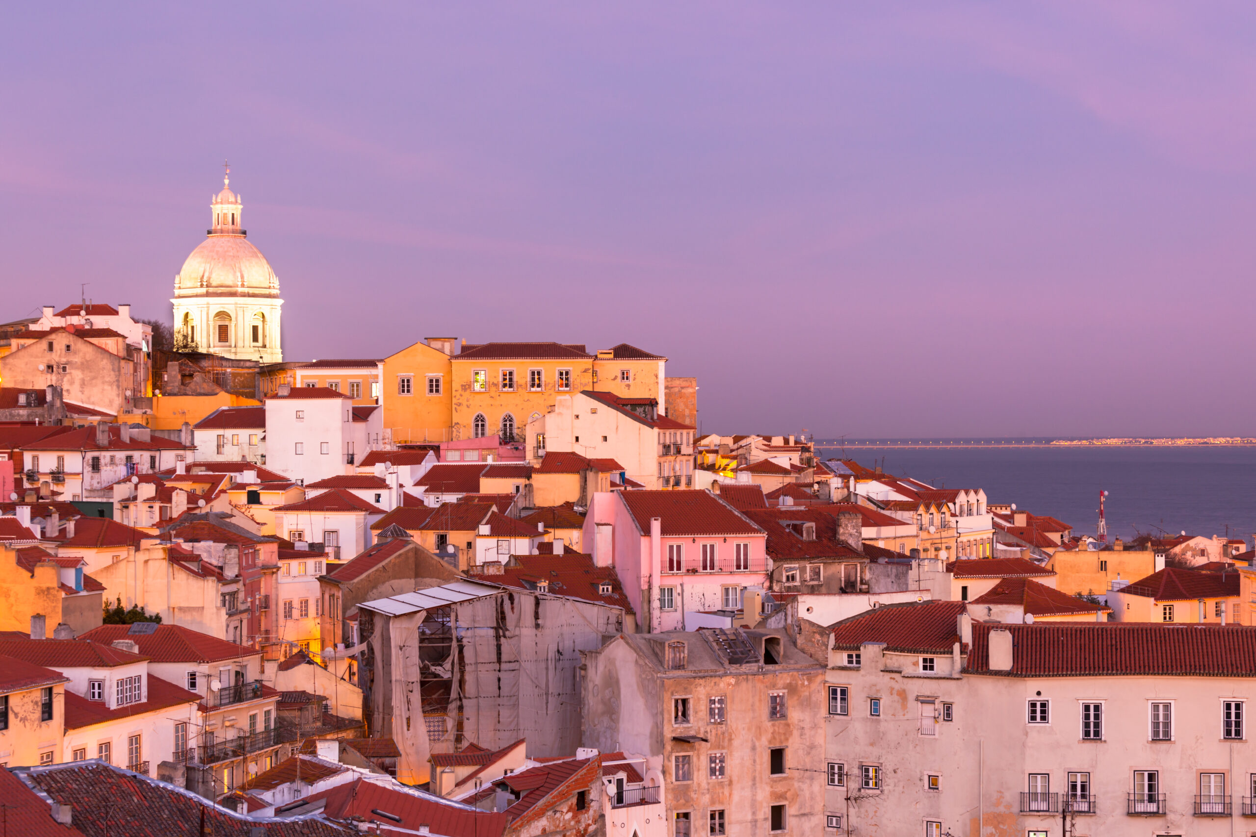 Panorama of old traditional city of Lisbon with red roofs and view of river Tagus at sunset